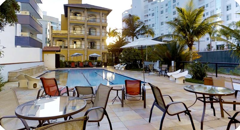 Fachada amarela do Hotel João de Barro vista da piscina, cercada por coqueiros