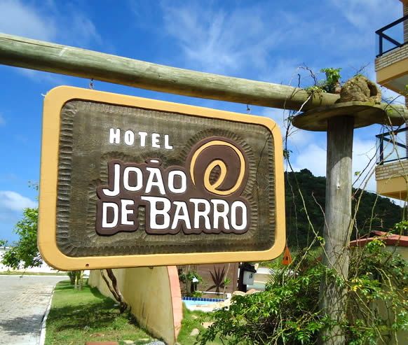 Placa de madeira do Hotel João de Barro entre a vegetação, com o morro ao fundo