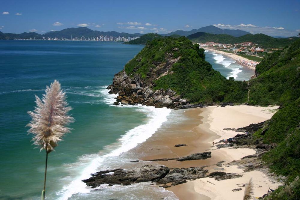 Praia da Solidão entre rochas e vegetação, com Balneário Camboriú ao fundo